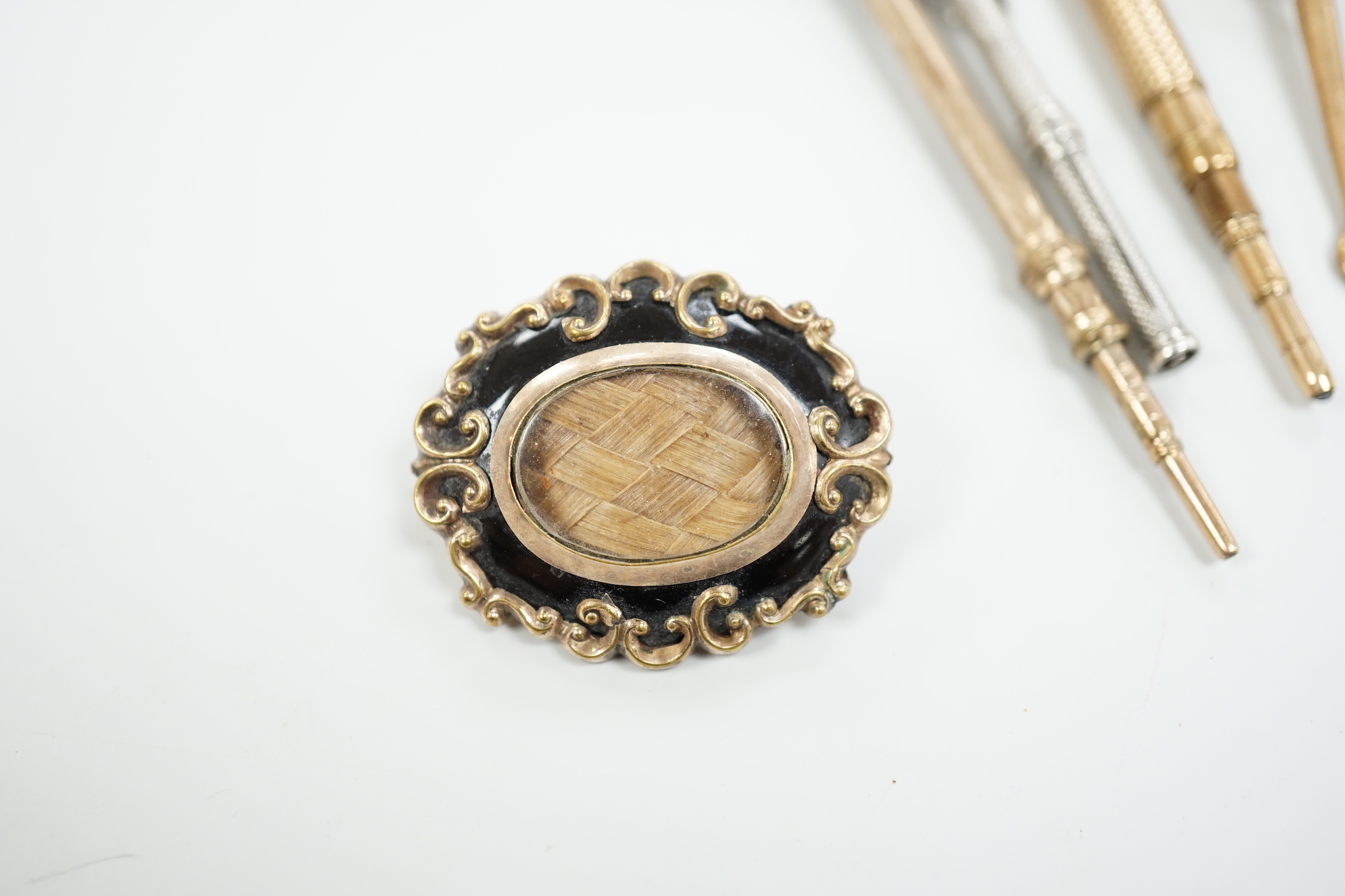 Four assorted early 20th century yellow or white metal overlaid propelling pencils, an agate set button hook, a two colour paste brooch and a Victorian enamelled mourning brooch, with plaited hair.